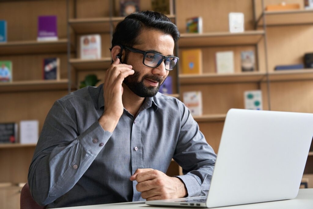 Indian customer support manager wearing headset consulting client on video call.